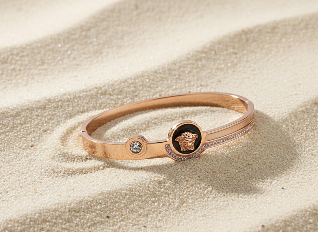 Rose gold bracelet with a central emblem on a sandy surface