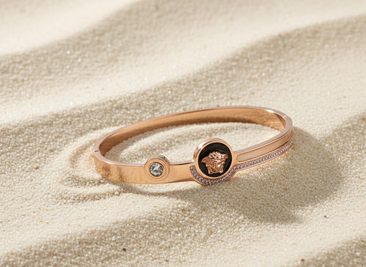 Rose gold bracelet with a central emblem on a sandy surface
